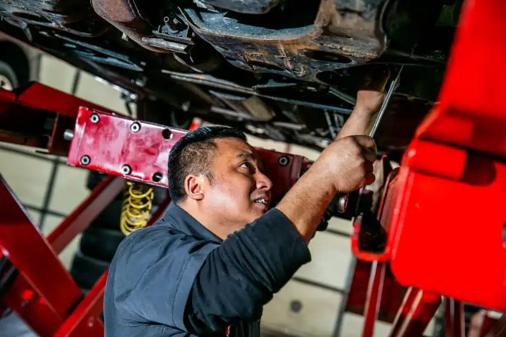 Ken's automotive and transmissions mechanic under car on lift with tool