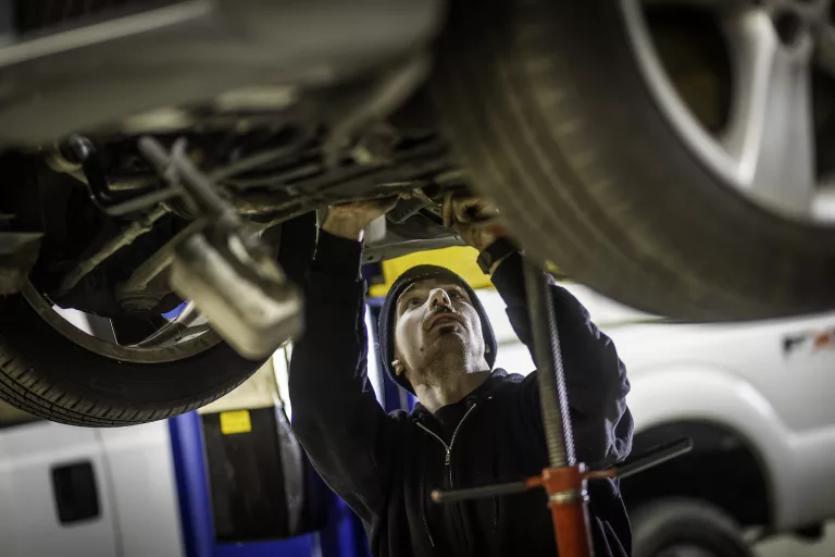 Ken's automotive and transmissions mechanic under car on lift with tool