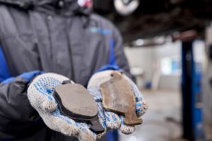mechanic holds a new and used brake pad side by side