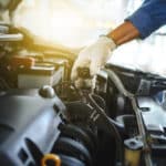 Young auto mechanic checks the water level in the radiator in the car. He was wearing white cloth gloves, holding the radiator cap.
