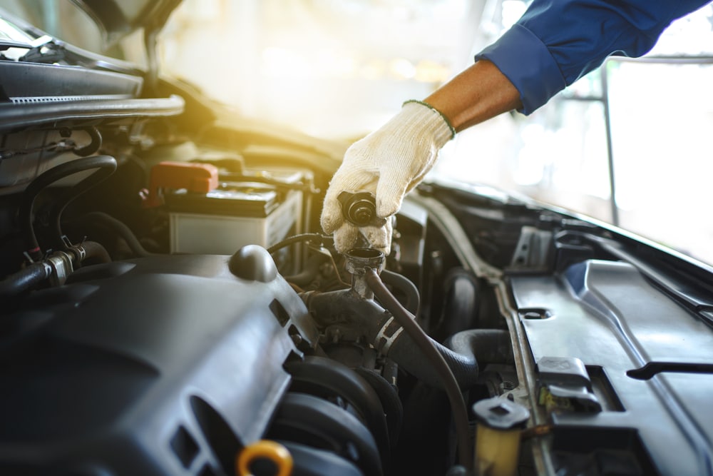 Why Preventative Maintenance Is More Important During Hot Weather 1 Young auto mechanic checks the water level in the radiator in the car. He was wearing white cloth gloves, holding the radiator cap.