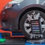 In the service station workshop, a car is on a stand with sensors on the wheels being checked for wheel alignment and camber.